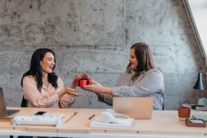 Female gives friend wrapped gift in an office setting. F2vfSB0