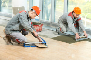 two workers cut and lay tile on a floor