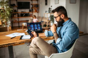 a person looking at stock charts on their smartphone with a laptop sitting on a table in the background