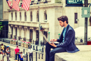 gettyimages man on laptop sitting on ledge across from wall street nyse