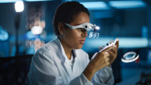 person in a white lab coat working with a circuit board