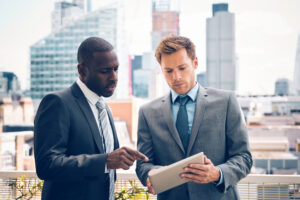 two people in suits reviewing a document while buildings loom in the background