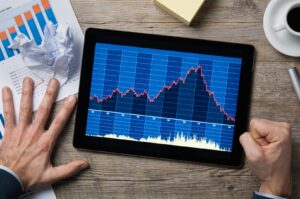man looking at declining share price chart on tablet and pounding fist on table stock loss bear mark