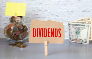 24 10 15 the word dividends held up between a jar of coins and paper money mf dload gettyimages 1324119709 1201x768 f5af3bb