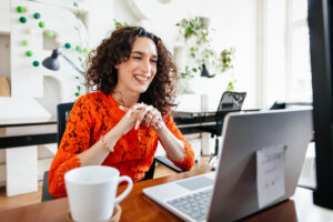 a person smiling while sitting at a table in front of a laptop computer