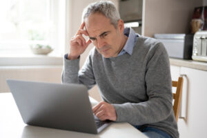 person sitting at table looking at a laptop in a worried manner
