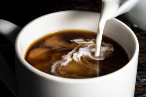 white liquid being poured into a brown beverage